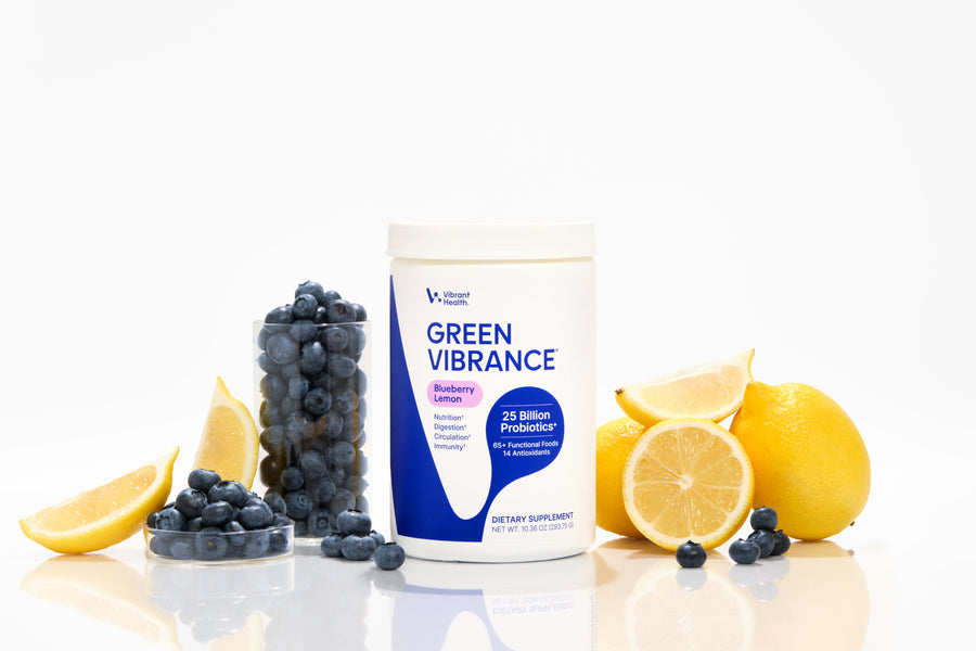 Green Vibrance Blueberry Lemon in a studio photo with fresh ingredients around the bottle on a white background.