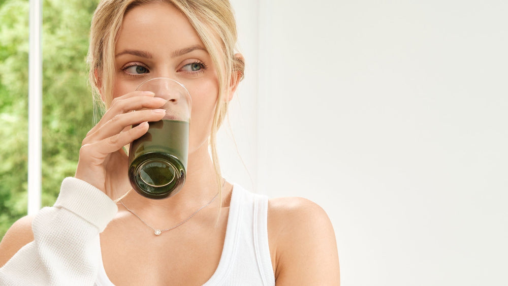 A young women wearing white clothing drinking super greens drink.
