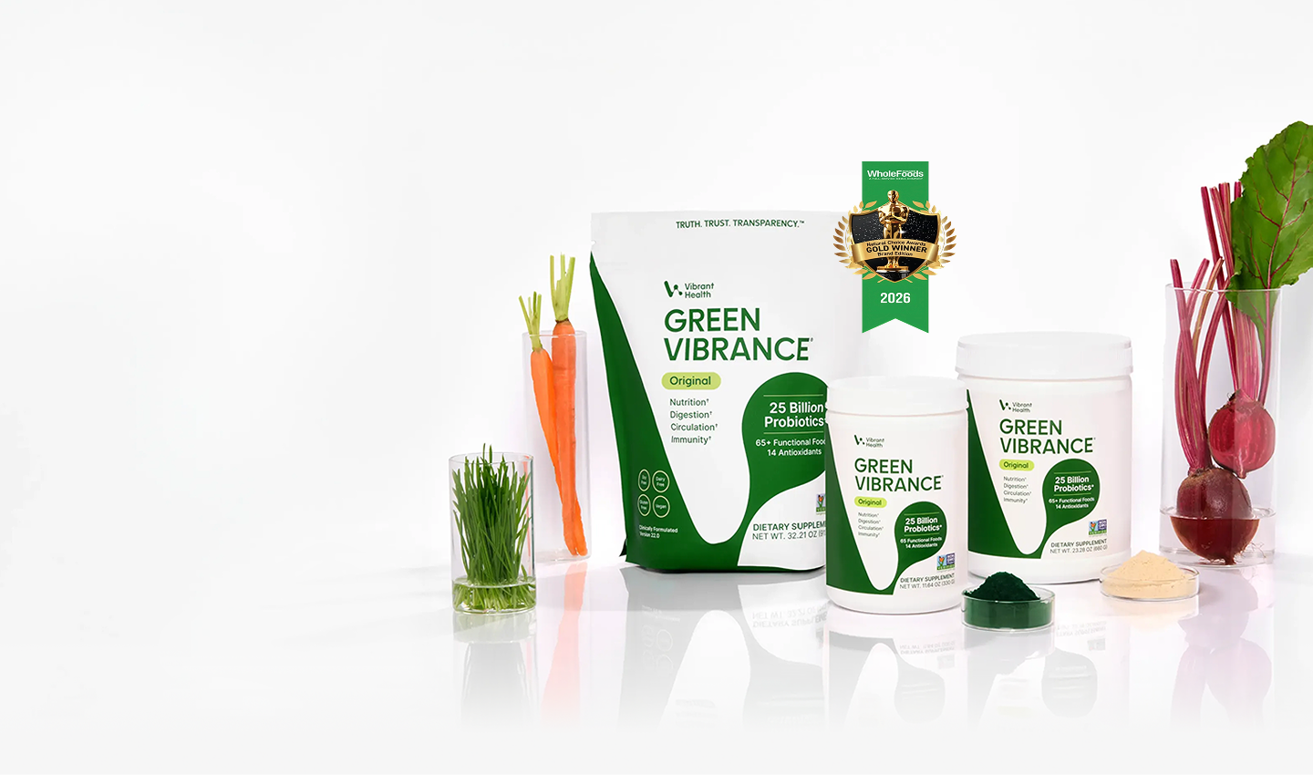 Vitality Labs Green Vibrance supplement products displayed on a white reflective surface with fresh vegetables including carrots, grass, and beets. A gold award badge for plant based greens powder.